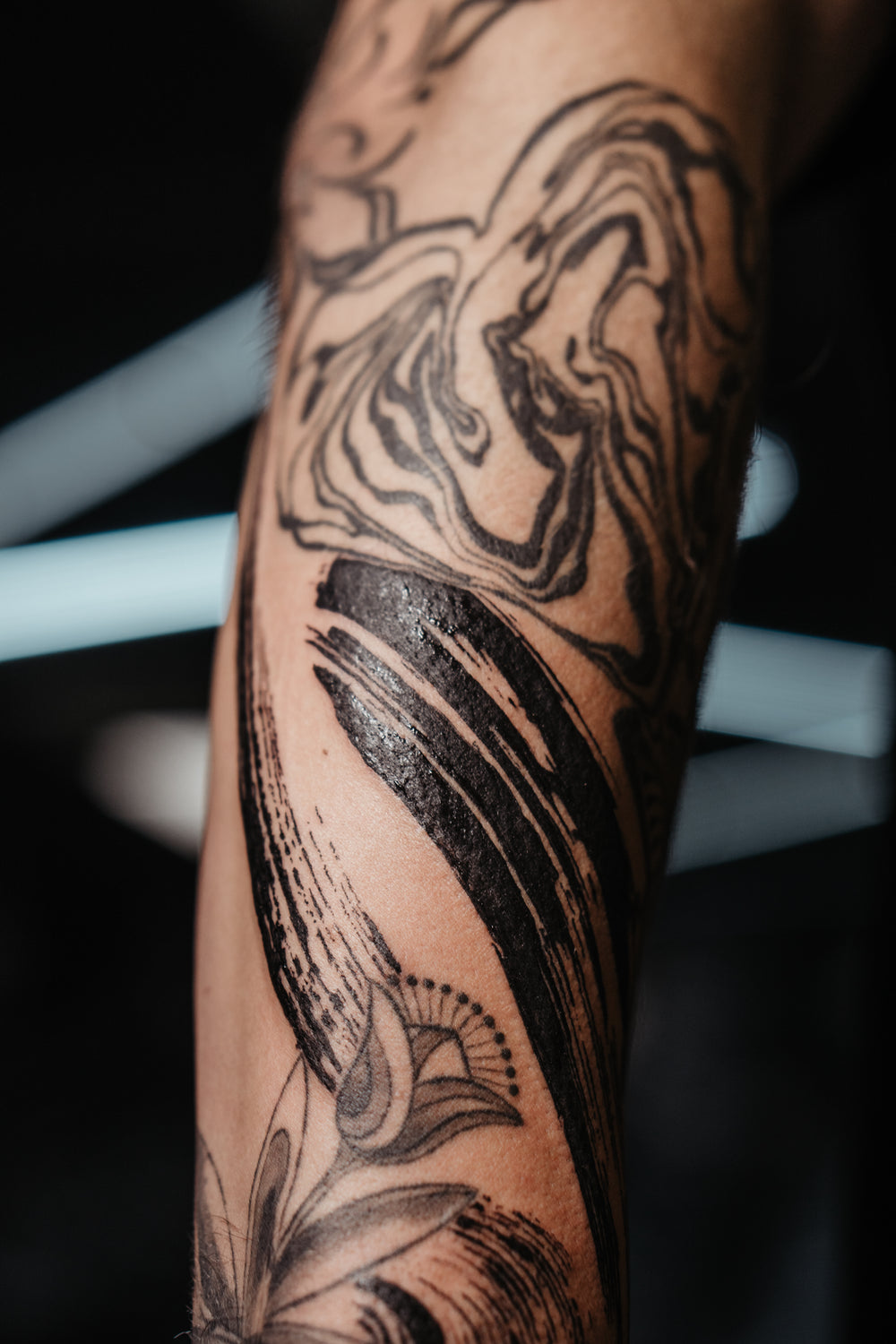 Close-up of a tattooed arm with intricate black ink designs on a blurred background
