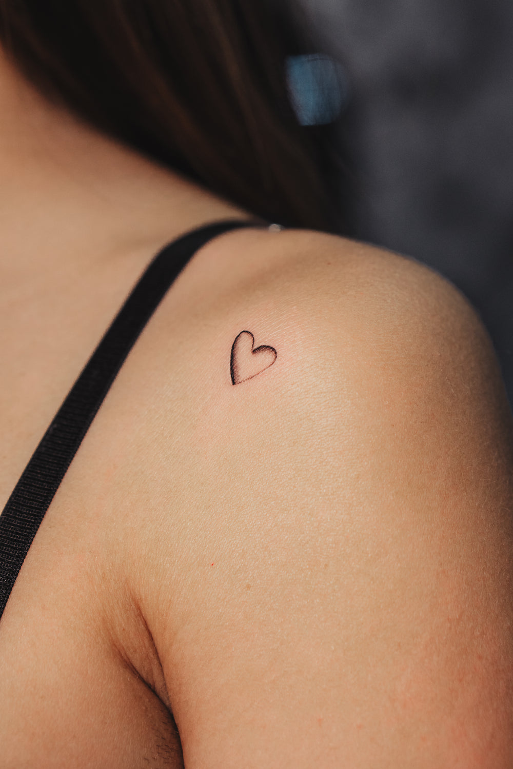 Small heart tattoo on a person's shoulder with a blurred background