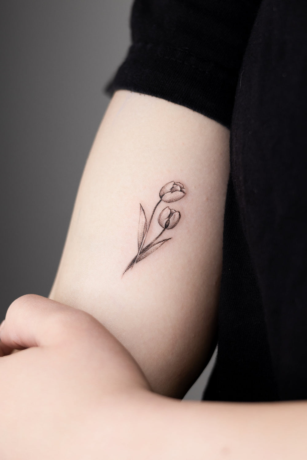 Small tattoo of a tulip on a person's arm against a dark background
