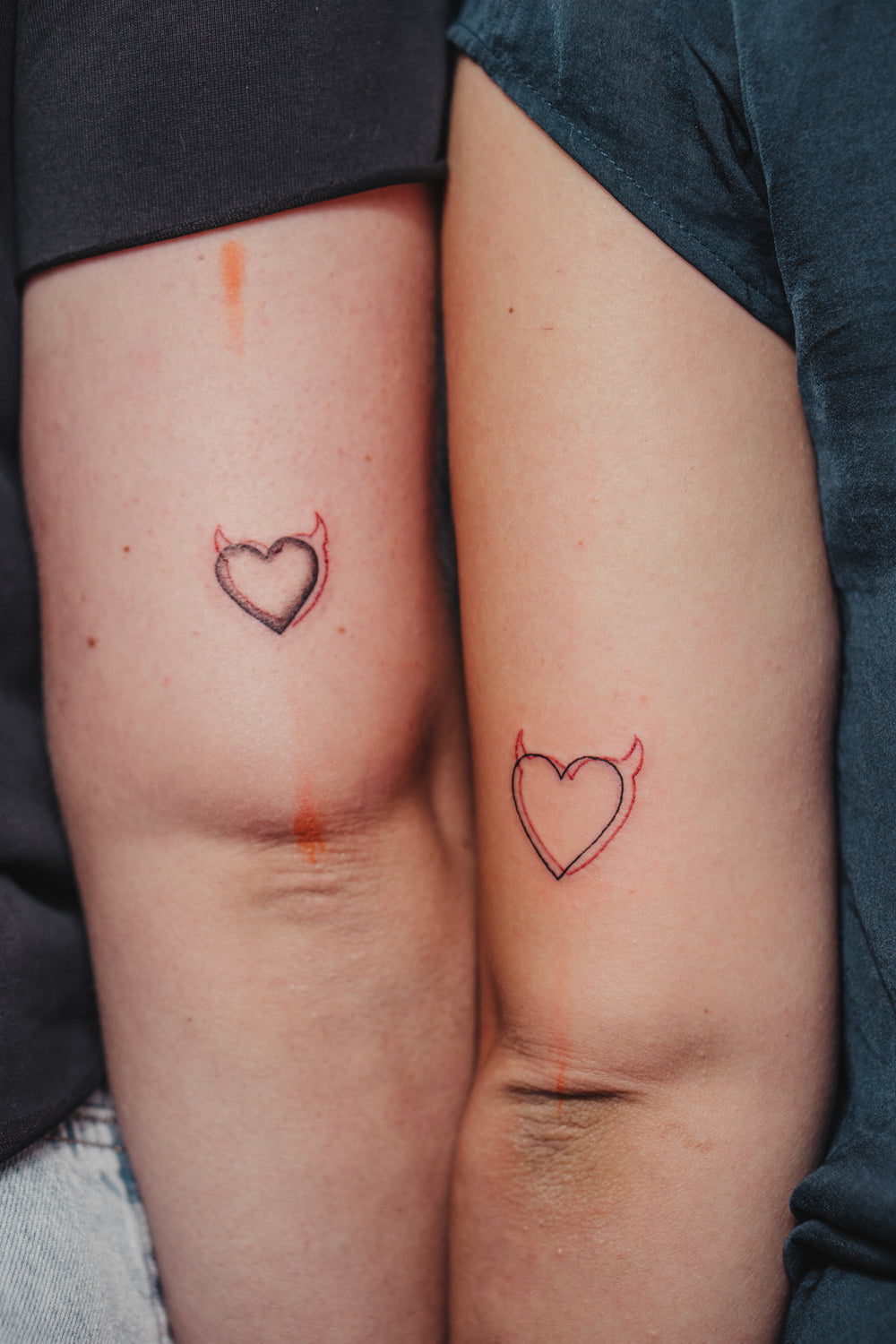 Two people with heart-shaped tattoos on their thighs.