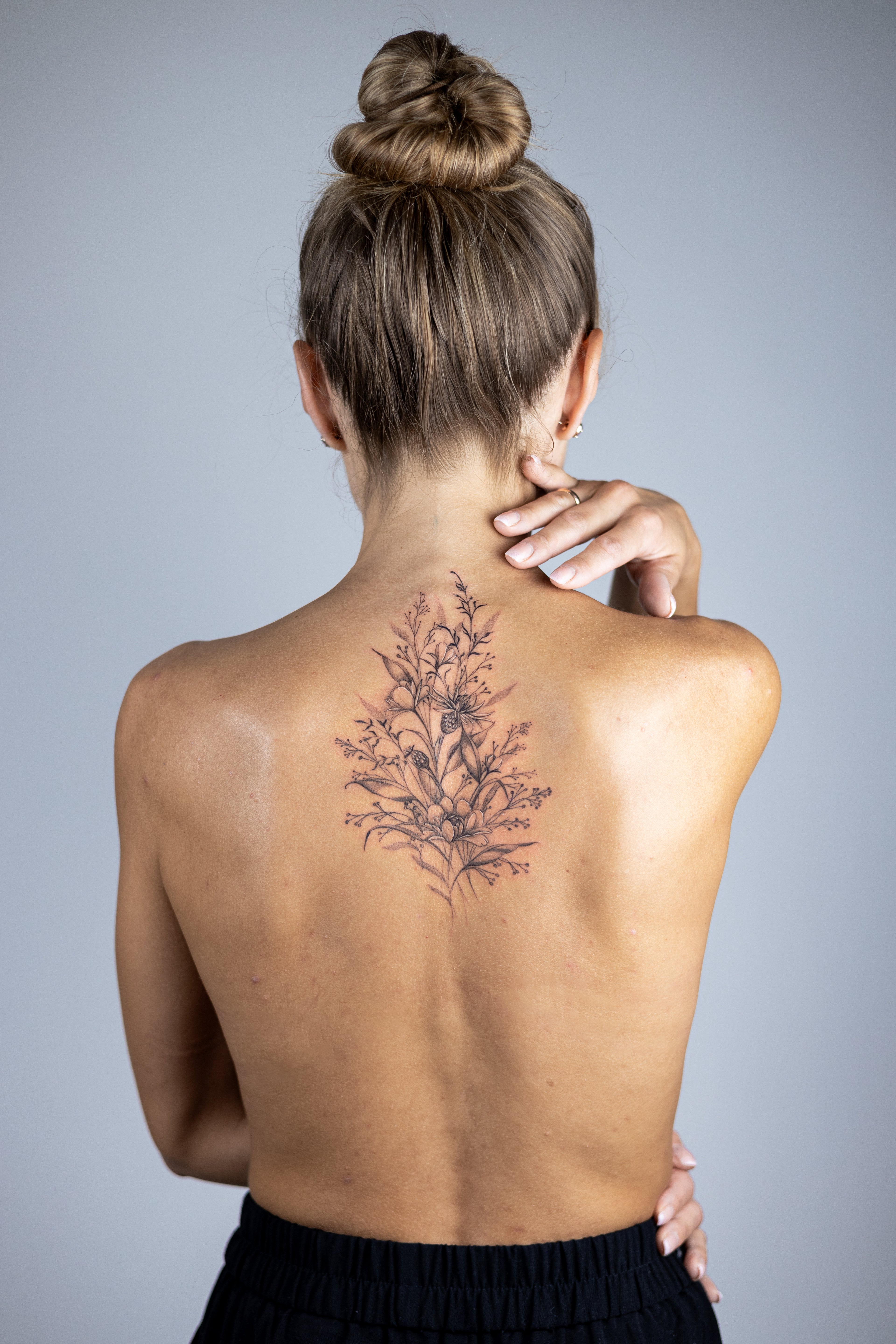 Woman with a floral tattoo on her back against a gray background